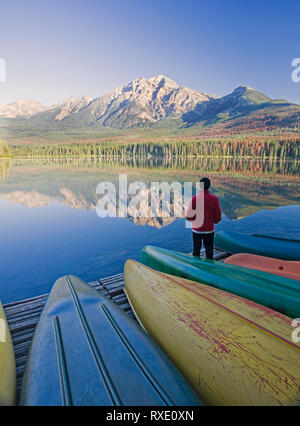 Einsame mittleren Alter Mann stehend auf Dock mit Kanus bei Pyramid Mountain im Pyramid Lake, Jasper National Park, Alberta, Kanada Stockfoto