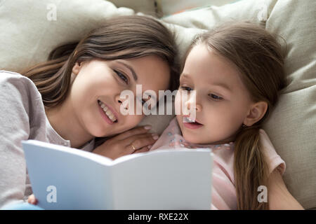 Glückliche Mutter hören Kind Tochter lernen Buch lesen im Bett Stockfoto