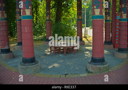 Rote hölzerne runde Bank in einem Park, der von großen roten Säulen umgeben Stockfoto