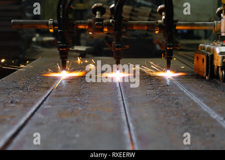 Die Maschine schneidet Bleche mit Gas. Flying spray geschmolzenes Metall. Seitenansicht. Drei gas- cutter Düsen Stockfoto