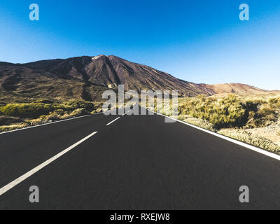 Langer Weg Straße am Berg mit Vulkan Mount vor und blue Clear Sky - Boden Sicht mit schwarzen Asphalt und weiße Linien - Fahren und tr Stockfoto