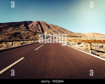 Langer Weg Straße am Berg mit Vulkan Mount vor und blue Clear Sky - Boden Sicht mit schwarzen Asphalt und weiße Linien - Fahren und tr Stockfoto