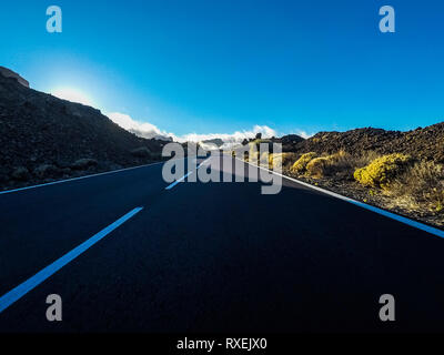 Langer Weg Straße am Berg mit Vulkan Mount vor und blue Clear Sky - Boden Sicht mit schwarzen Asphalt und weiße Linien - Fahren und tr Stockfoto