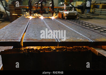 Die Maschine schneidet Bleche mit Gas. Flying spray geschmolzenes Metall. Seitenansicht. Drei gas- cutter Düsen Stockfoto