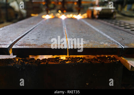 Die Maschine schneidet Bleche mit Gas. Flying spray geschmolzenes Metall. Seitenansicht. Drei gas- cutter Düsen Stockfoto