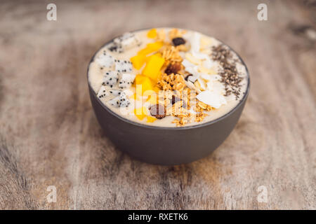 Smoothie Schüsseln mit Mango, Banane, Granola, Kokosraspeln, Dragon Obst, Chia Samen und Minze auf Holz- Hintergrund. Konzept Früchte, Vitamine. Stockfoto