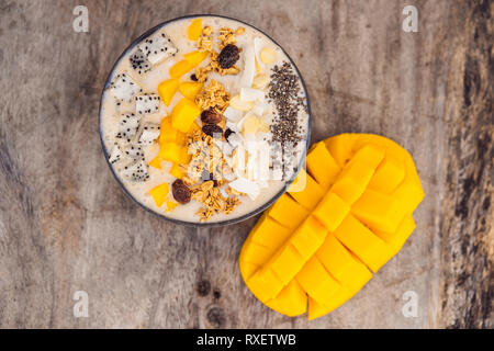 Smoothie Schüsseln mit Mango, Banane, Granola, Kokosraspeln, Dragon Obst, Chia Samen und Minze auf Holz- Hintergrund. Konzept Früchte, Vitamine. Stockfoto