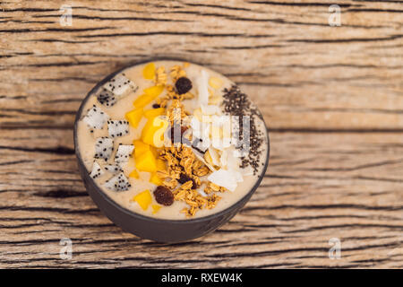 Smoothie Schüsseln mit Mango, Banane, Granola, Kokosraspeln, Dragon Obst, Chia Samen und Minze auf Holz- Hintergrund. Konzept Früchte, Vitamine. Stockfoto