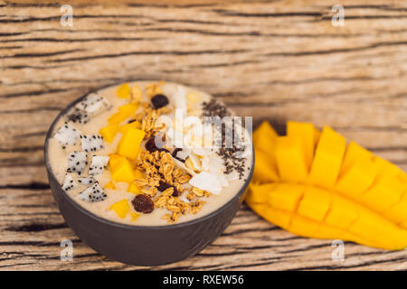 Smoothie Schüsseln mit Mango, Banane, Granola, Kokosraspeln, Dragon Obst, Chia Samen und Minze auf Holz- Hintergrund. Konzept Früchte, Vitamine. Stockfoto