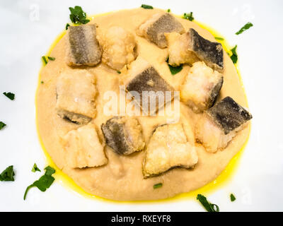 Italienische Küche - Blick von oben auf die Stücke von Baccala (Stockfisch) mit Creme von Kichererbsen auf weiße Platte in einem lokalen Restaurant in der Lombardei Stockfoto