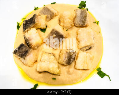 Italienische Küche - Blick von oben auf die Stücke von Baccala (Stockfisch) mit pürierten Kichererbsen schließen bis auf weiße Platte in einem lokalen Restaurant in der Lombardei Stockfoto