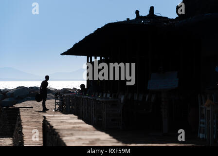 Silhouetten von Gebäuden und Menschen stehen auf einem Pier, den Ozean und den blauen Himmel im Hintergrund Stockfoto