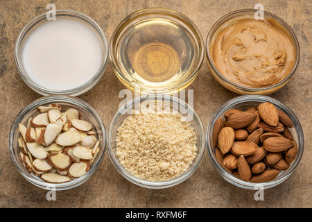 Sammlung von Mandel super Foods: Nüsse, Mehl, Schichten, Milch, Öle und Butter - Blick von oben auf die kleine Glasschalen über strukturierte Rinde Papier Stockfoto