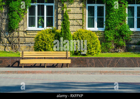 Die städtische Invironment - Holzbank vor dem Backstein Fassade eines alten Gebäudes bedeckt mit Efeu. Elemente der Verschönerung in der Architektur. livi Stockfoto