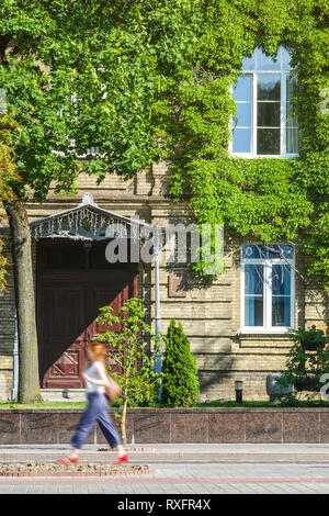 Backstein Fassade eines alten Gebäudes bedeckt mit Efeu. Die Abbildung einer Person zu Fuß verschwommen in Bewegung. Elemente der Verschönerung in der Architektur. Stockfoto