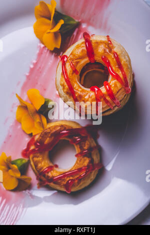 Vertikale Foto mit Top Aussicht auf mehreren Donuts aus Blätterteig Teig. Red Topping Erdbeer ist auf Ringe verschüttet. Donuts sind auf weißem Pla platziert Stockfoto