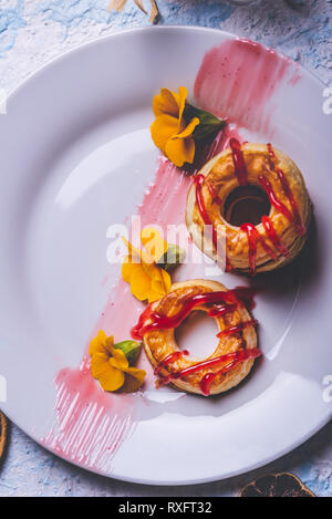 Vertikale Foto mit Top Aussicht auf mehreren Donuts aus Blätterteig Teig. Red Topping Erdbeer ist auf Ringe verschüttet. Donuts sind auf weißem Pla platziert Stockfoto