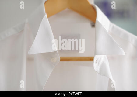 Nahaufnahme Detail des weißen Hemdes hängt auf braunen hölzernen Kleiderbügel Stockfoto