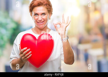 Senior kaukasische Frau mit roten Herzen in Liebe über isolierte Hintergrund tun ok Zeichen mit den Fingern, ausgezeichnete Symbol Stockfoto