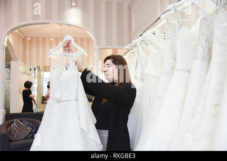 2 Verkäuferinnen helfen, eine hübsche rothaarige Mädchen in einer Wedding Dress Shop Ihr Traum Kleid abholen Stockfoto