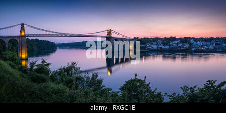 Die Menai Bridge über die Menai Strait und Stadt Menai Bridge bei Dämmerung, Anglesey, North Wales, UK Stockfoto