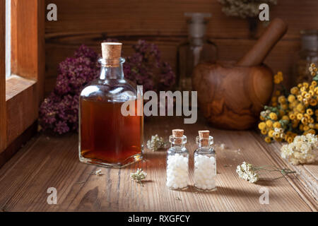 Zwei Flaschen homöopathische Globuli mit getrockneten Kräutern und eine Tinktur im Hintergrund Stockfoto