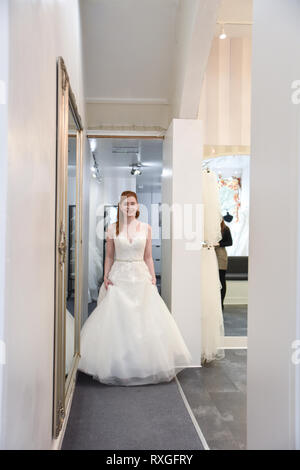 Eine hübsche rothaarige Mädchen ist in einer Wedding Dress Shop suchen t und versuchen, auf weiße Brautkleider Stockfoto