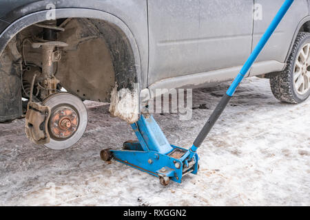 Die Arbeiten zur Beseitigung der Räder aus dem Auto auf der Straße im Winter. Austausch der Winterreifen für den Sommer mit einem Wagenheber. Stockfoto