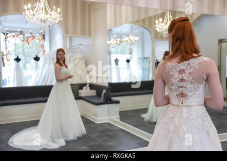 Eine hübsche rothaarige Mädchen ist in einer Wedding Dress Shop suchen t und versuchen, auf weiße Brautkleider Stockfoto