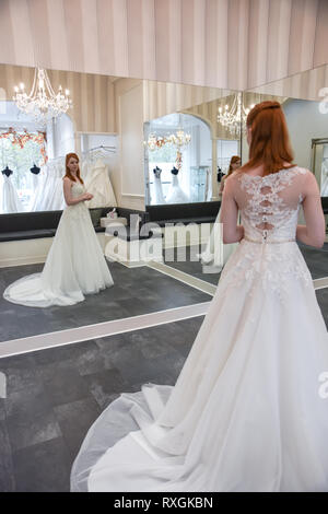 Eine hübsche rothaarige Mädchen ist in einer Wedding Dress Shop suchen t und versuchen, auf weiße Brautkleider Stockfoto