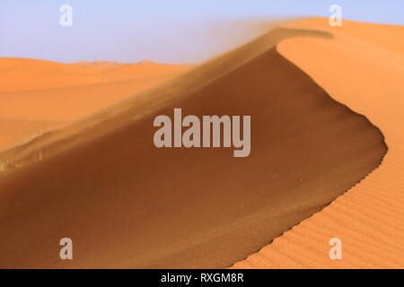 Dünen ridge Detail, blauer Himmel. Orange Sand Wellen und Textur. Sand im Wind Hintergrund. Sahara. Marokko. Stockfoto