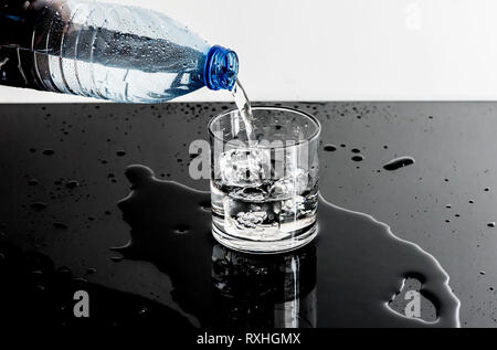 Kunststoff Flasche gießt Wasser in ein Glas Stockfoto