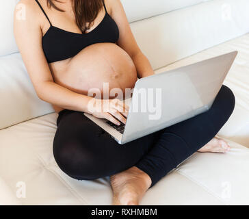 Schwangere Frau mit Bauch mit einem Laptop auf dem Sofa Stockfoto