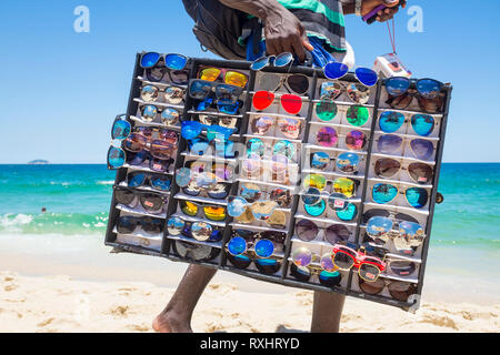 RIO DE JANEIRO - Februar 10, 2017: Ein afrikanischer Einwanderer Verkauf gefälschter Sonnenbrille geht mit einer Vitrine für Kunden am Strand von Ipanema. Stockfoto