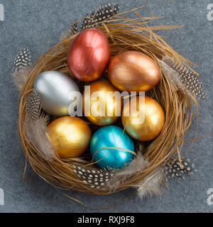 Frohe Ostern Urlaub gruss Symbol stilvollen natürlichen Holz- Gras Nest mit bunten Wachtel Eier und Federn auf grauem Stoff Hintergrund Stockfoto