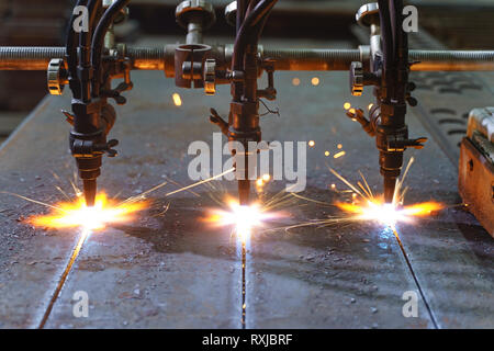 Die Maschine schneidet Bleche mit Gas. Flying spray geschmolzenes Metall. Seitenansicht. Drei gas- cutter Düsen Stockfoto