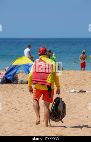 Freiwillige männliche Surf rescue Person zu Fuß über bilgola Beach in Sydney die Surf rescue Schwimmweste, Sydney, Australien Stockfoto