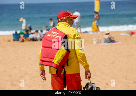 Freiwillige männliche Surf rescue Person zu Fuß über bilgola Beach in Sydney die Surf rescue Schwimmweste, Sydney, Australien Stockfoto