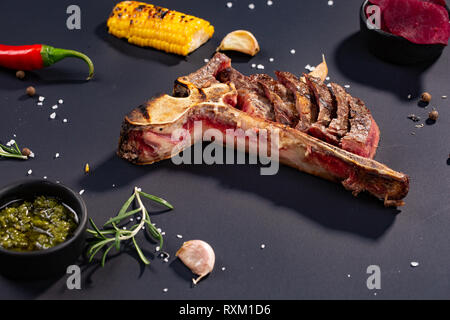 Eingestellt von Gegrilltem geschnittenes T-Bone Steak mit gegrilltem Mais, Sauce, Chili, Rosmarin, Salz, Knoblauch auf schwarzem Hintergrund. Nach und nach Hinzufügen Fleischstücke Stockfoto