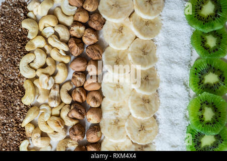 Frische Zutaten für eine gesunde Rohkost Frühstück. Kiwi, Kokosraspeln, Cashews und Haselnüsse Schuß von oben, Zutaten für einen Smoothie Schüssel Stockfoto