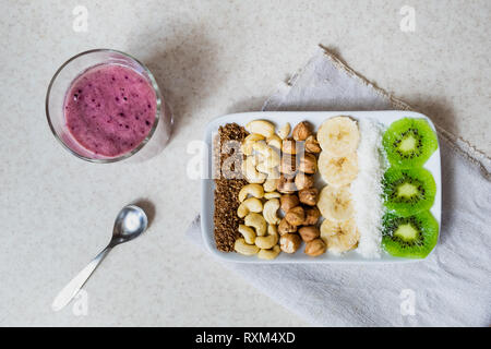 Frische Zutaten für eine gesunde Rohkost Frühstück. Kiwi, Kokosraspeln, Cashews und Haselnüsse Schuß von oben, Zutaten für einen Smoothie Schüssel Stockfoto