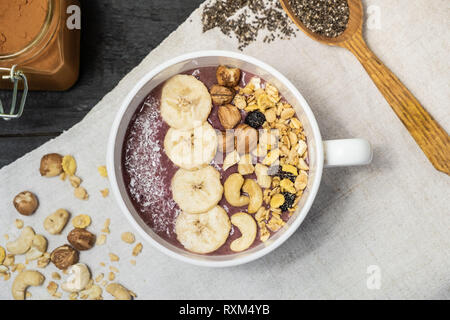 Schale mit Obst Smoothie, Nüsse und Bananen, Ansicht von oben. Flach eines acai Schüssel mit Getreide, Cashews und Haselnüsse auf Vintage rustikalen Tisch Stockfoto