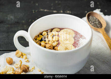 Schale mit Obst Smoothie, Nüsse und Bananen. Acai Schüssel mit Getreide, Cashews und Haselnüsse auf Vintage rustikalen Tisch Stockfoto