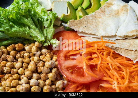 Nahaufnahme der Buddha Schüssel auf einem rustikalen Tisch. Vegane Mahlzeit aus Kichererbsen, Salat, Gemüse, Tofu, Fladenbrot und Avocado Stockfoto