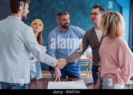 Froh, mit Ihnen zu arbeiten! Junge moderne Männer in Smart Casual Wear Hände schütteln und lächelnd, während in der kreativen Arbeiten im Büro. Stockfoto