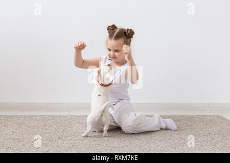 Pet's Besitzer, Kinder und Hunde Konzept - kleines Mädchen auf dem Boden sitzend mit niedlichen Jack Russell Terrier Welpen und Spielen Stockfoto