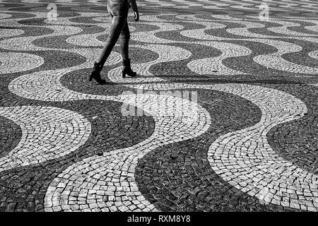 Die Beine einer Frau zu Fuß über die berühmte Wave gemusterten Kopfsteinpflaster, Rossio, Lissabon, Portugal, Schwarz und Weiss Stockfoto