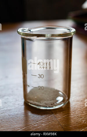 Close-up Seitenansicht 40 mL Chemie Becher mit kleinen Tabelle Zucker Kristalle gefüllt. Licht aus gefangen, die den oberen Rand der Becher. Stockfoto