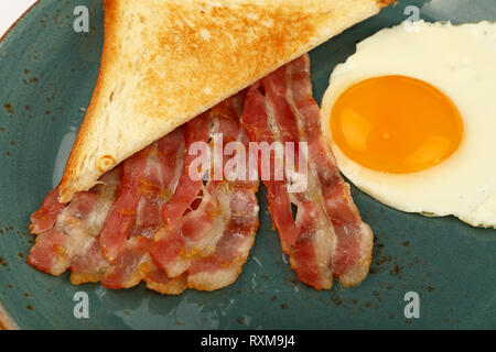 Nahaufnahme, englisches Frühstück, sonnigen Seite Ei, Toast und gebratenem Speck Schichten auf blauen Platte, hohe Betrachtungswinkel Stockfoto