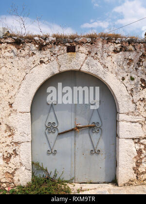 Alte gekrümmte lackiertem Metall Tür auf Stone Fence unter blauem Himmel mit einigen Wolken. Stockfoto